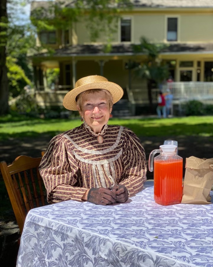 Woman sitting at a table outdoors and wearing a Victorian costume.